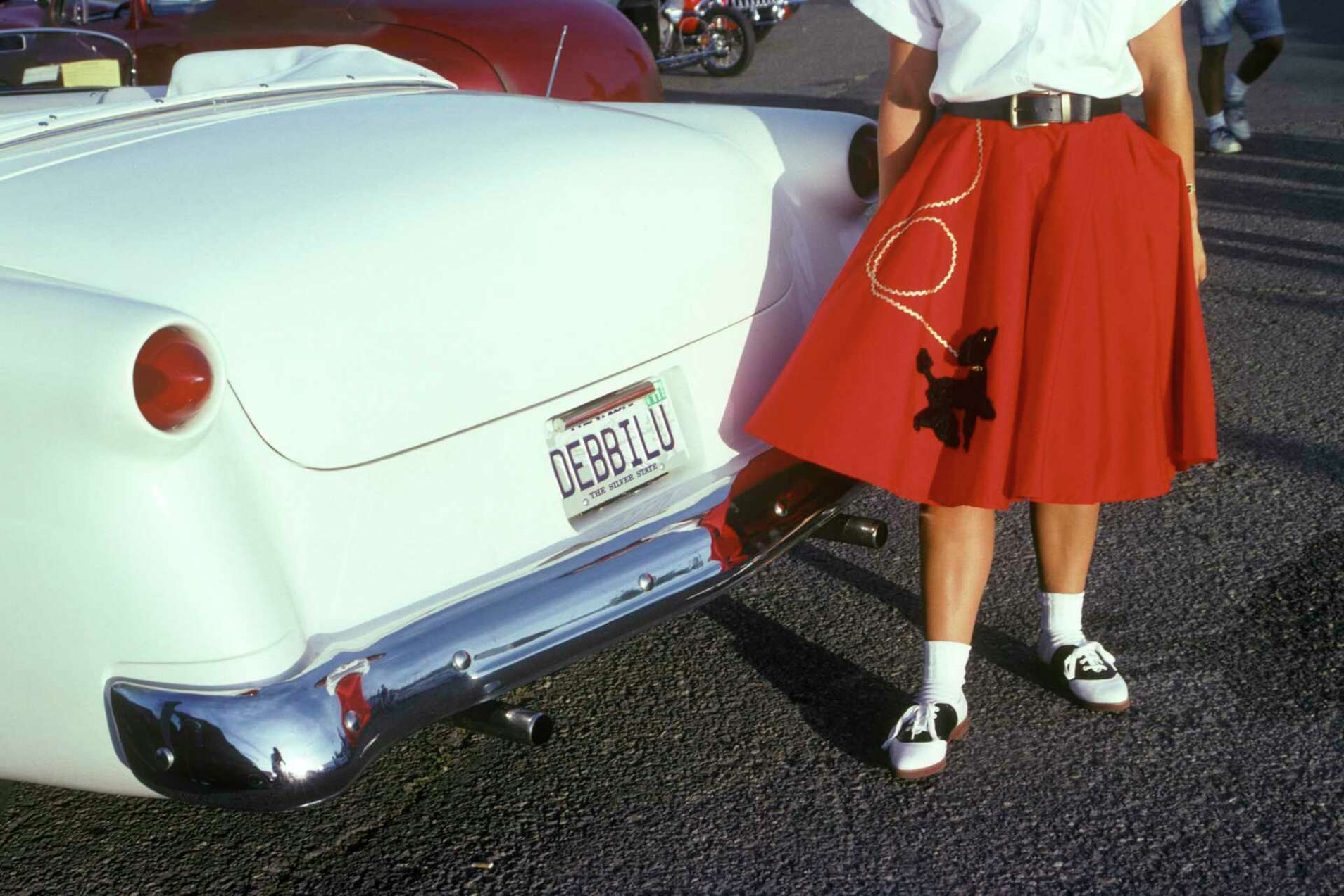 Vintage white car fins and a woman in a red poodle skirt, showing how AI image to music captures retro 1950s aesthetics.