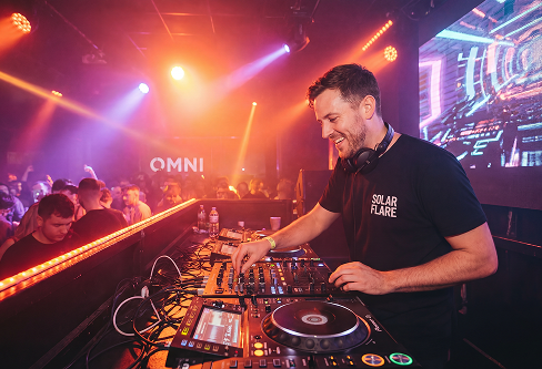 Smiling DJ performing live at a vibrant nightclub, seamlessly mixing tracks in perfect harmony using a handy Audio Key Finder